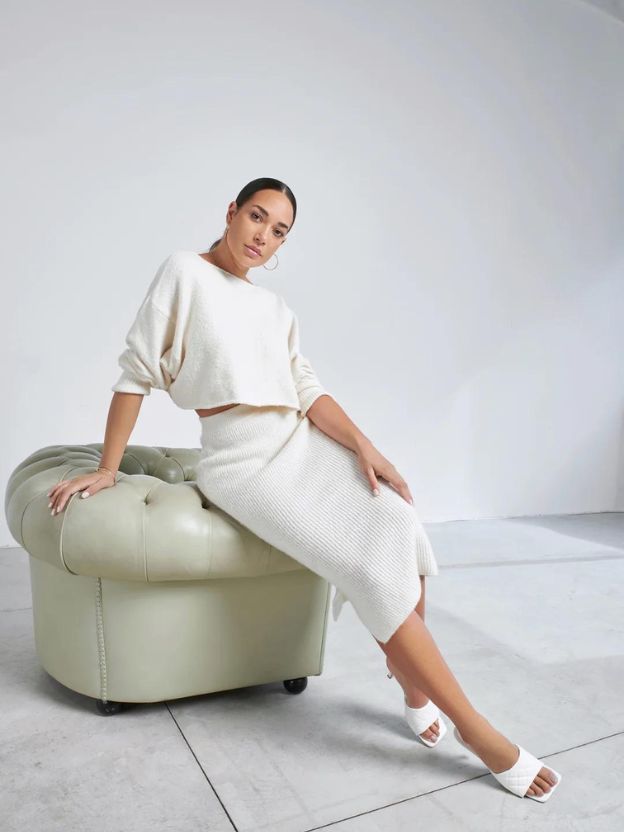 woman sitting on the armrest of an armchair dressed in white tenne blouse and midi skirt