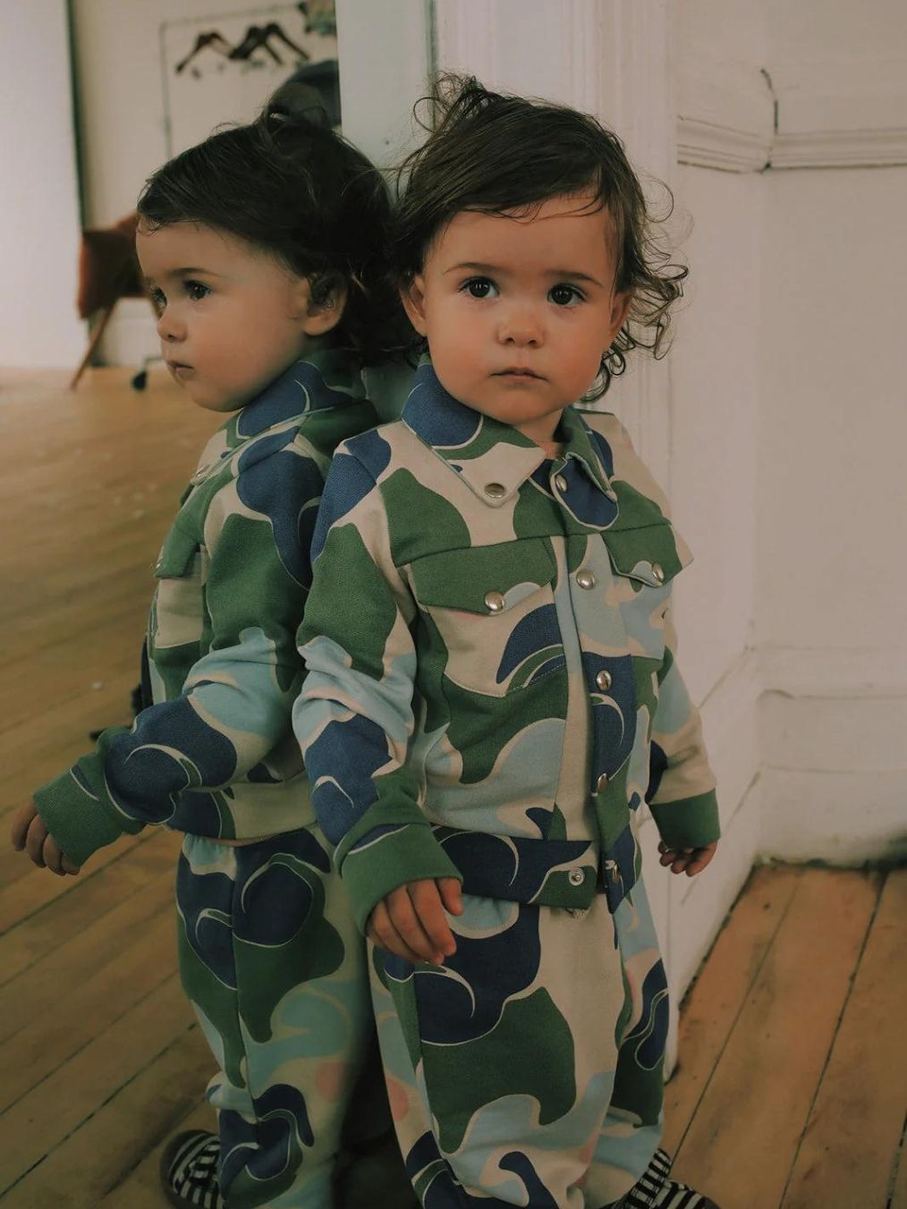 Lapsi seisoo kotona peiliin nojaten päällään sinivihreä granelito takki ja housut