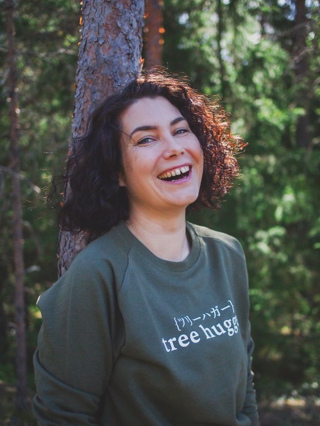 Nainen nojaa puuhun metsässä nauraen päällään Metsä/Skogen vihreä tree hugger collegepaita
