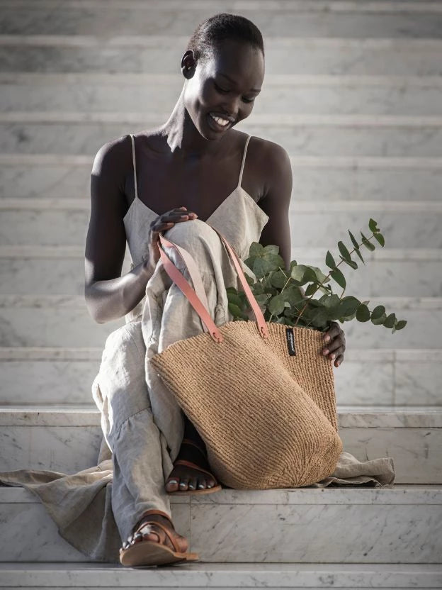 Woman smiling and sitting on stairs with handmade woven bag
