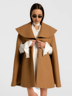 Woman wearing a brown cape over a white outfit on a light gray background