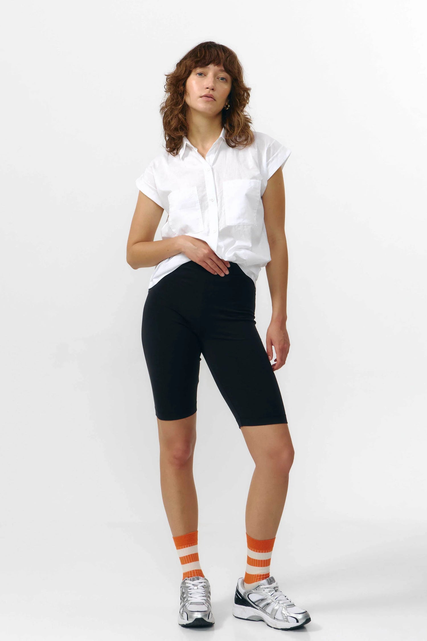 Woman wearing a white shirt, black capri pants, and orange socks with white stripes on a white background