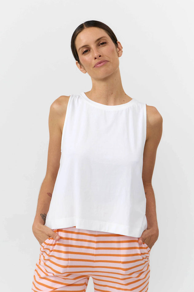 Woman wearing a white sleeveless top and orange striped pants on a white background