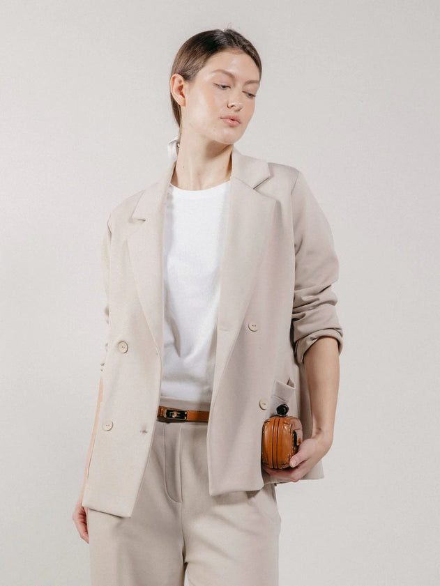 Person wearing a beige blazer and pants holding a small pumpkin against a plain background