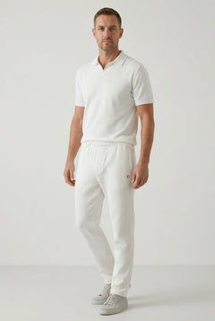 Man wearing a white polo shirt and pants on a light gray background