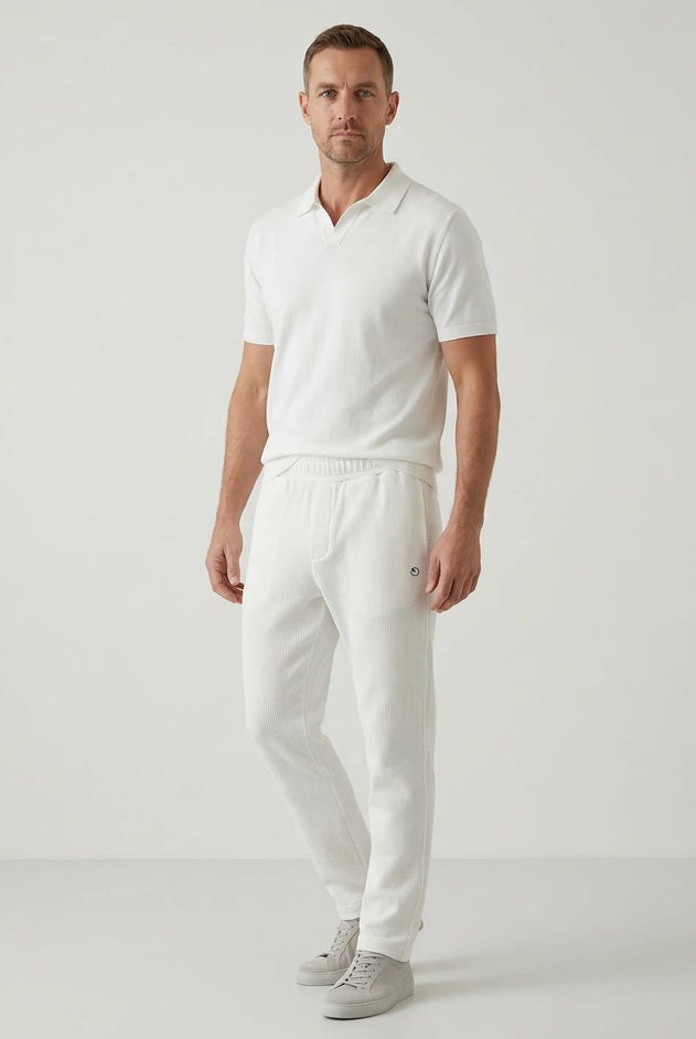 Man wearing a white polo shirt and pants on a light gray background