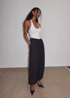 Woman wearing a white top and black pants against a plain background