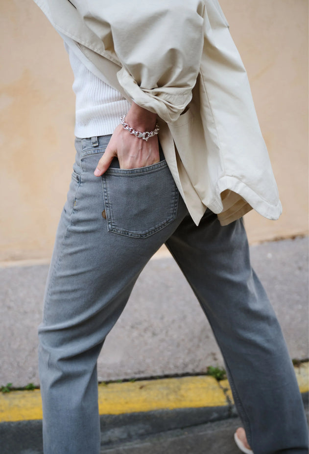 Person wearing a beige jacket and gray jeans with a blurred background