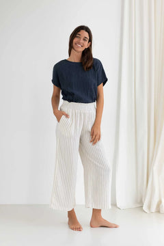 Woman wearing a navy top and white striped pants standing against a white curtain.