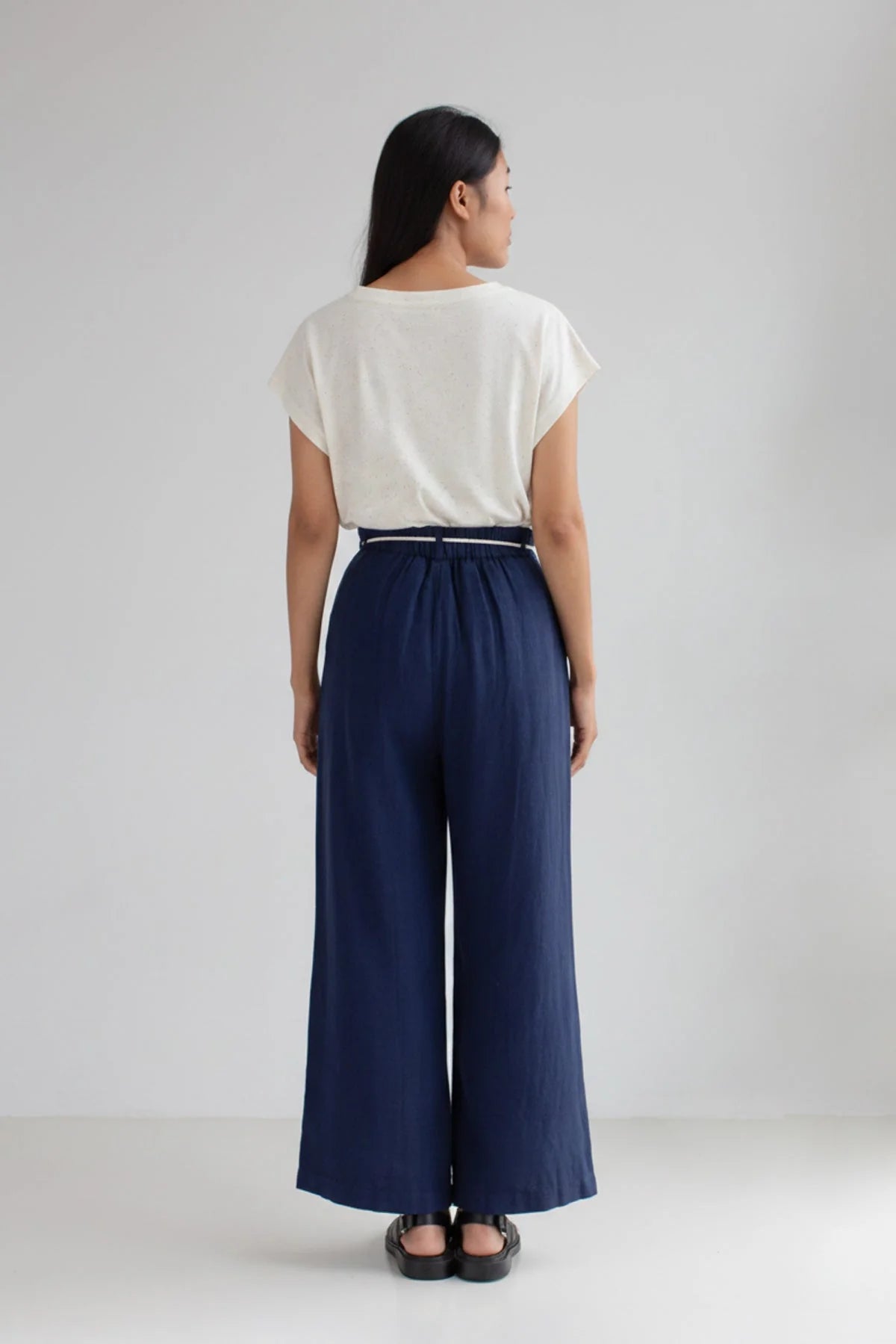 Person wearing a white top and navy wide-leg pants on a plain background