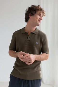 Man wearing a brown striped polo shirt with a small logo, standing against a white background.