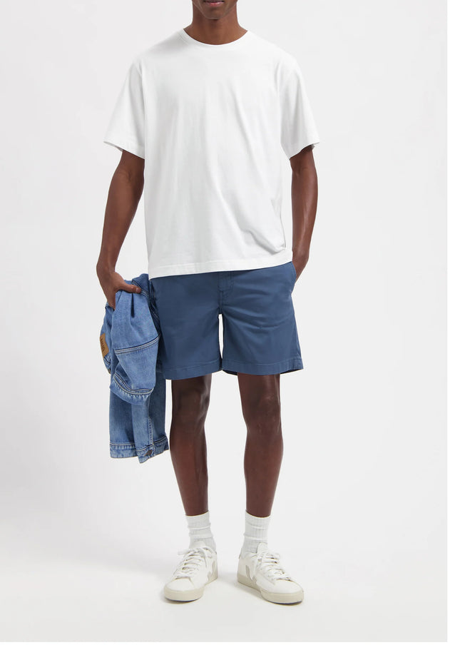 Person wearing a white t-shirt and blue shorts holding a denim jacket on a white background