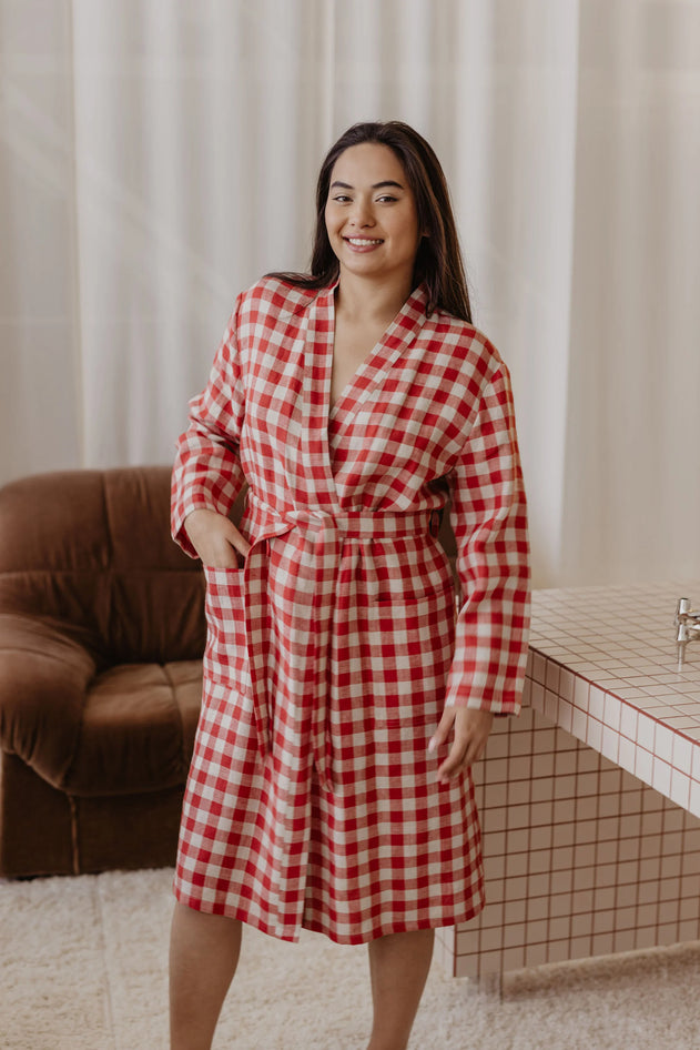 Woman wearing a red and white checkered dress standing in a room with a brown couch and tiled wall.