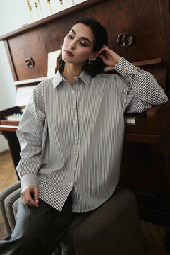 Woman wearing a striped shirt sitting in a room with wooden furniture.