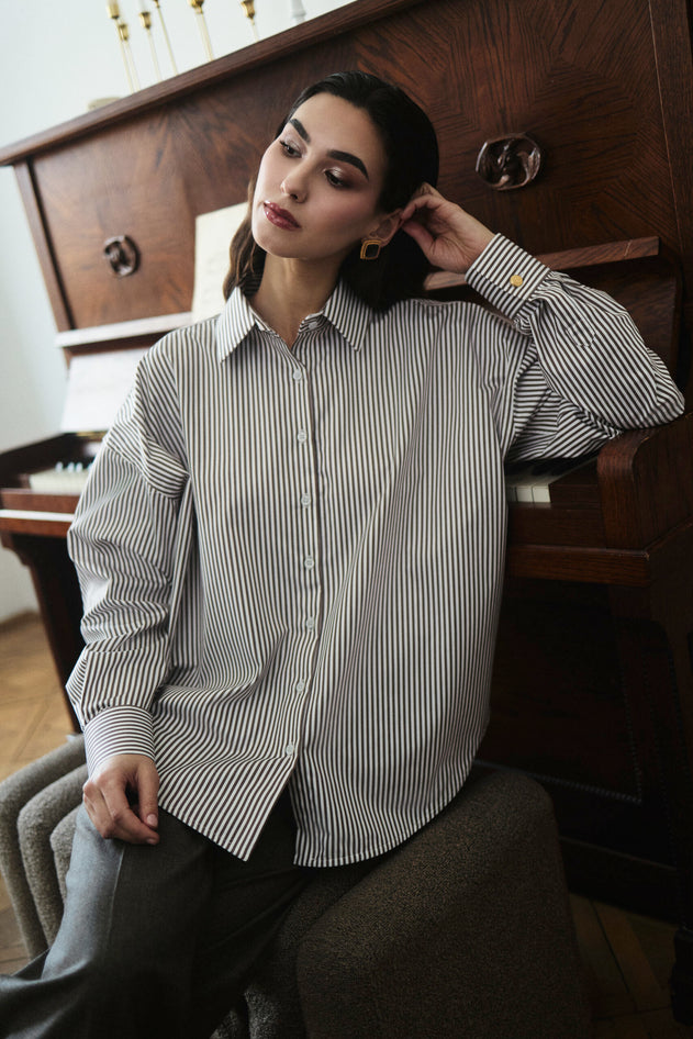 Woman wearing a striped shirt sitting in a room with wooden furniture.