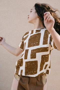 Woman wearing a brown and white patterned shirt against a beige wall