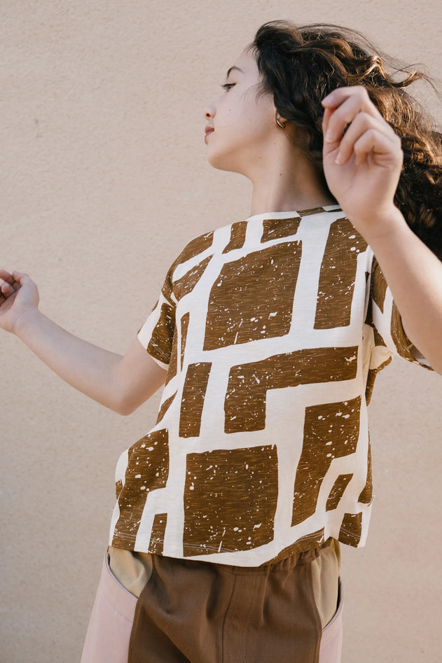 Woman wearing a brown and white patterned shirt against a beige wall