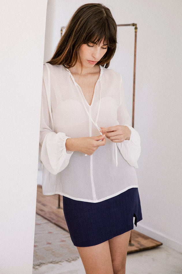 Woman wearing a white blouse and navy skirt in a minimal indoor setting
