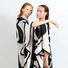 Two women wearing black and white patterned dresses against a plain background