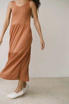 Person wearing a rust-colored dress with white sneakers on a light wooden floor.