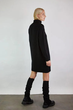 Woman wearing a black dress and knee-high boots against a plain background