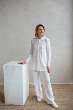 Woman in a white lace outfit standing next to a white cube against a plain wall.