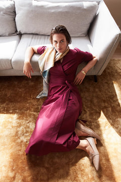 Woman in a burgundy dress sitting on a beige carpet in a living room.