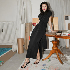 Woman in a black dress standing in an artist's studio with art supplies and furniture.