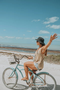 Woman riding a bicycle on a beach with a clear blue sky.