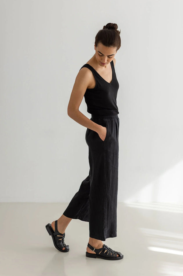 Woman wearing a black sleeveless top and wide-leg pants on a white background