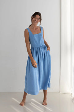 Woman wearing a blue dress standing in a bright room with white walls.