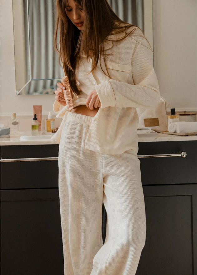 Woman in a cream ribbed lounge set standing in a bathroom.