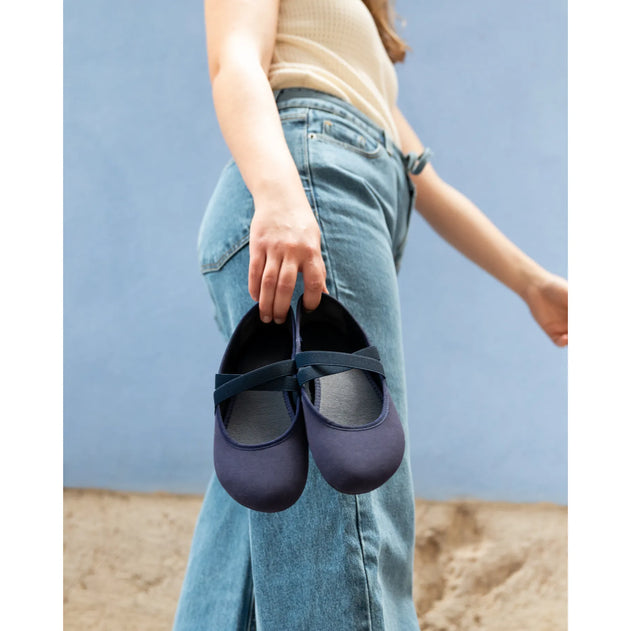 Person holding a pair of navy flats against a blue background