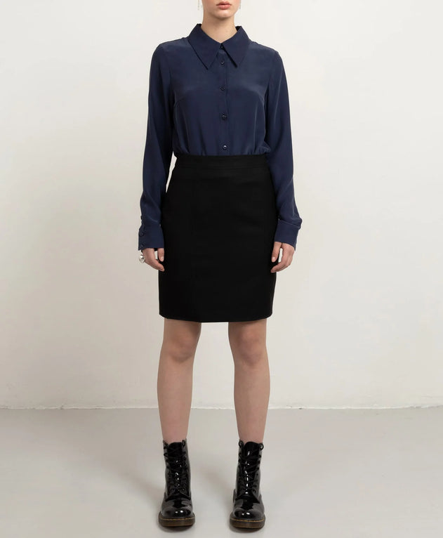 Person wearing a navy shirt, black skirt, and black boots on a white background