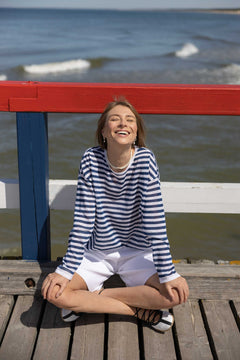 Woman sitting on a wooden pier by the water, smiling.