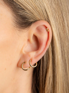 Close-up of an ear wearing gold hoop earrings with blonde hair.