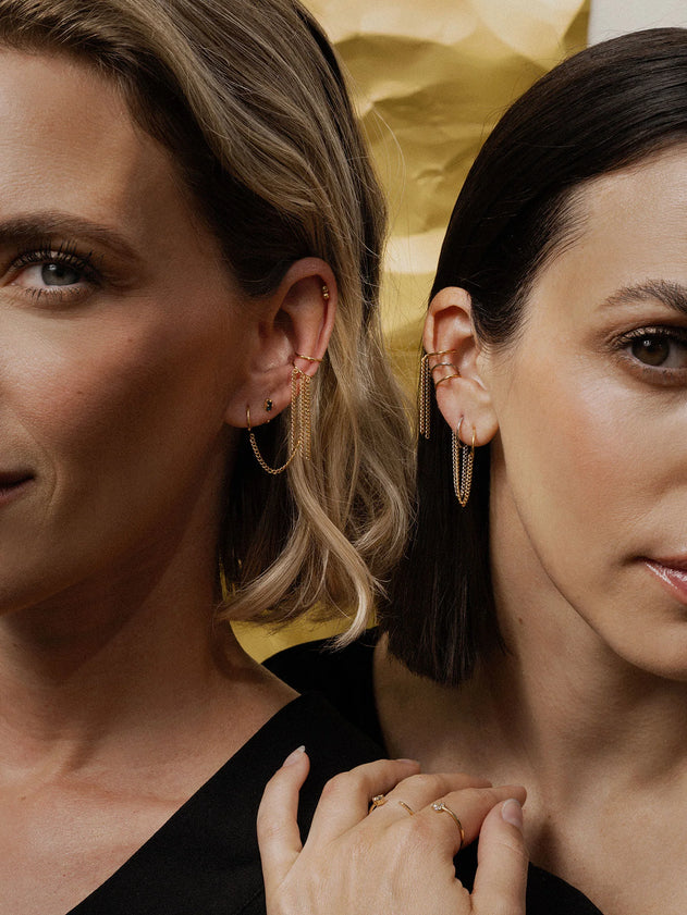 Two women wearing gold hoop earrings with a neutral background