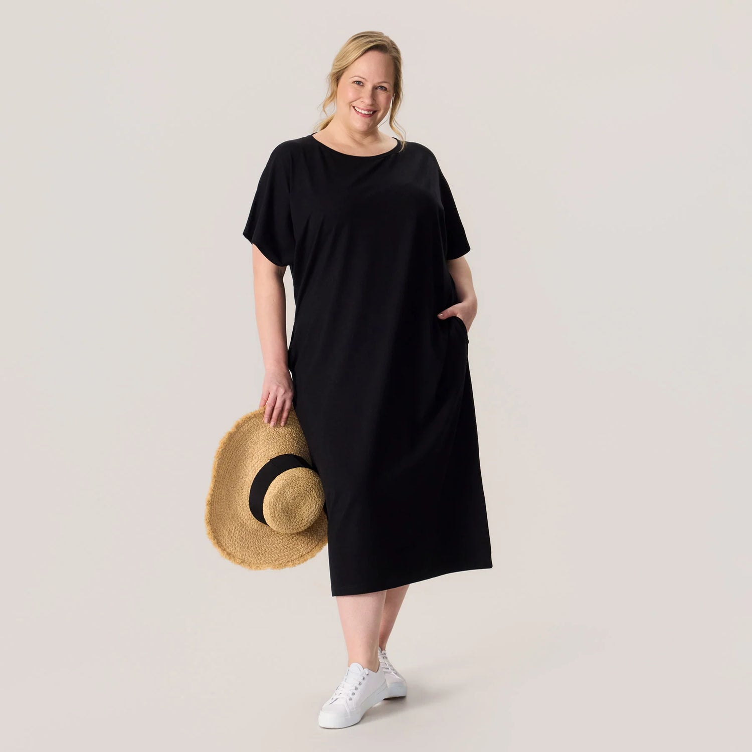 Woman wearing a black dress holding a straw hat on a plain background