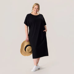 Woman wearing a black dress holding a straw hat on a plain background
