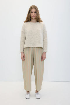 A model stands against a plain white studio background wearing a light beige knit sweater, beige and cream vertically striped wide-leg cropped trousers, and white sneakers.
