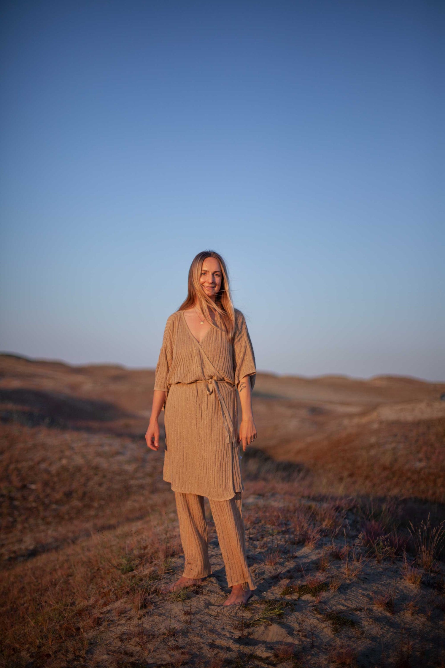 Woman in a beige dress standing in a desert landscape with clear blue sky