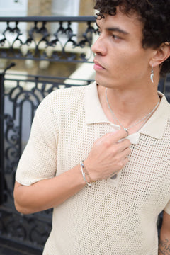 Man wearing a beige knit polo shirt with a decorative metal railing in the background