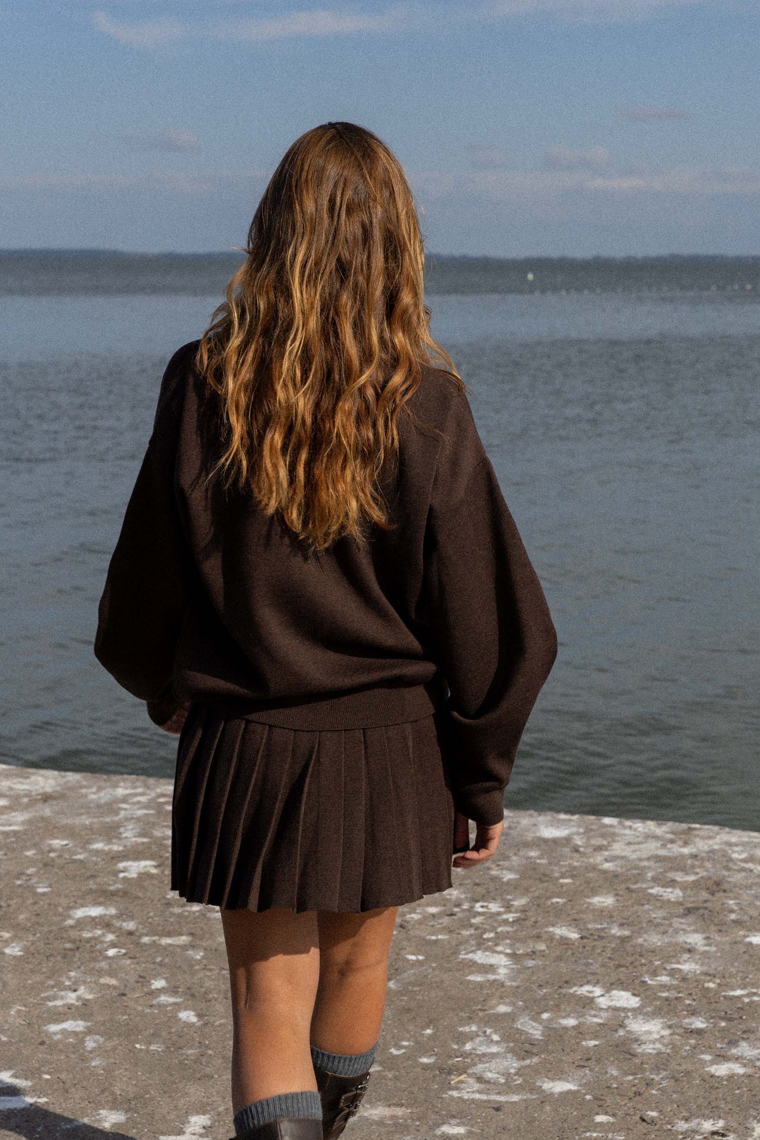 Person wearing a brown outfit standing by a body of water