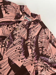 The SPINDRIFT - Organic Cotton Shirt - Pink Wave features a pink and brown abstract wave print, button-up design, Komodo label on the collar, and is laid flat on a white surface.